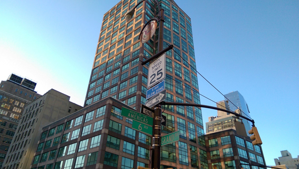 A photo of the street sign showing the intersection of Grand Street and Avenue of the Americas with a rusty plaque of the USA on top