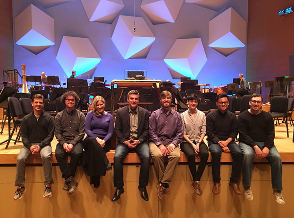Kevin Puts and the seven 2016 Minnesota Orchestra Institute Composers sitting on the edge of the orchestra stage/