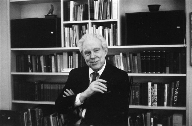 Elliott Carter standing in front of a bookcase (1982).