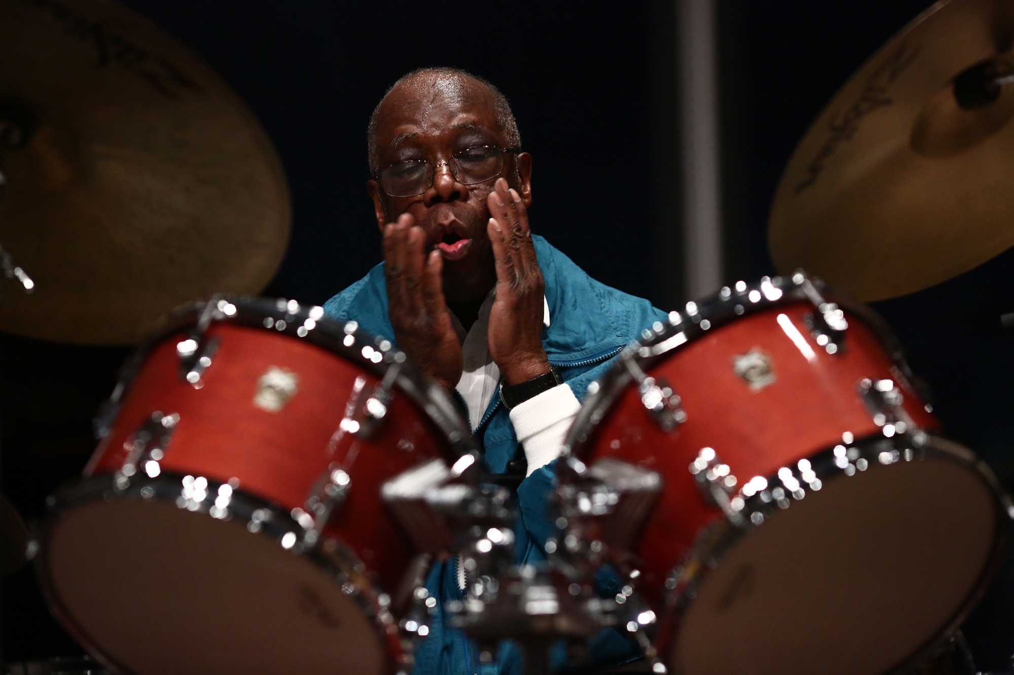 Andrew Cyrille with his hands on his cheeks in front of a drum set at his solo performance during Open Plan: Cecil Taylor, April 16 2016 at The Whitney Museum of American Art. Photograph © Paula Court, courtesy Whitney Museum of American Art