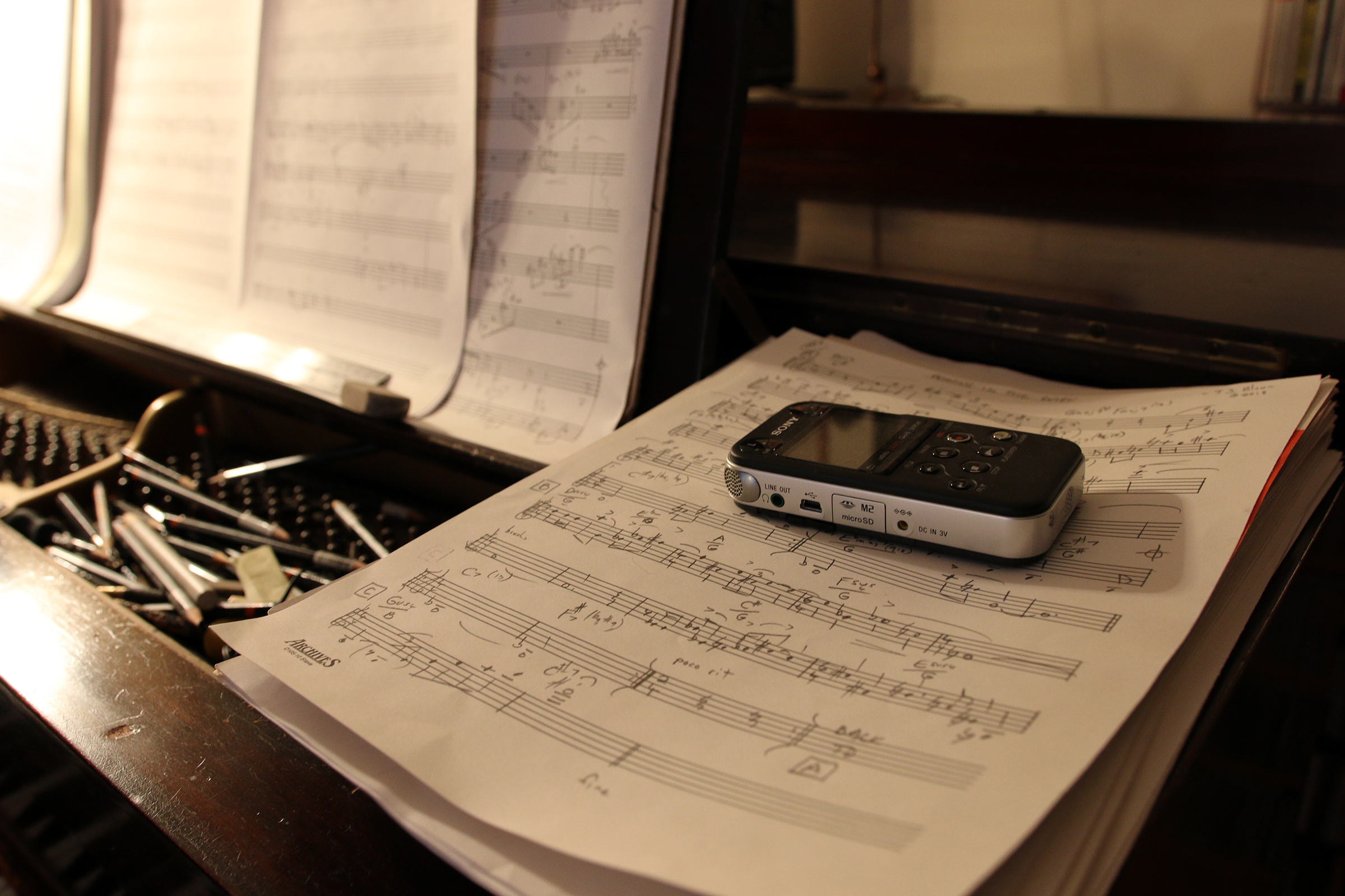 A pocket-sized audio-recorder on a pile of music manuscript paper in one of the corners on the right hand corner of Jane Ira Bloom's grand piano.