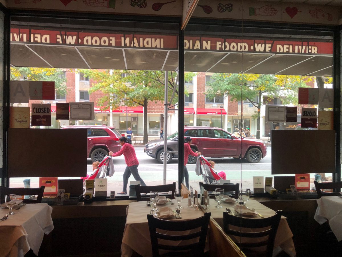 A baby cart and a car moving as seen from a window from within a restaurant, and their reflections through a mirror.