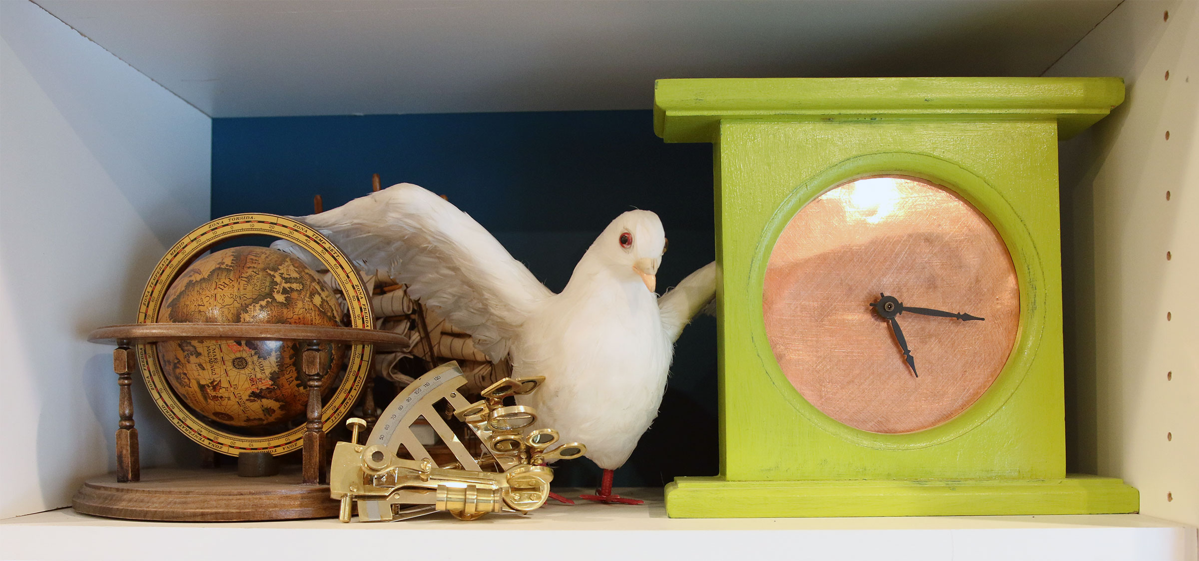 A globe, a compass, a statue of a bird, and a clock crammed into a small shelf.