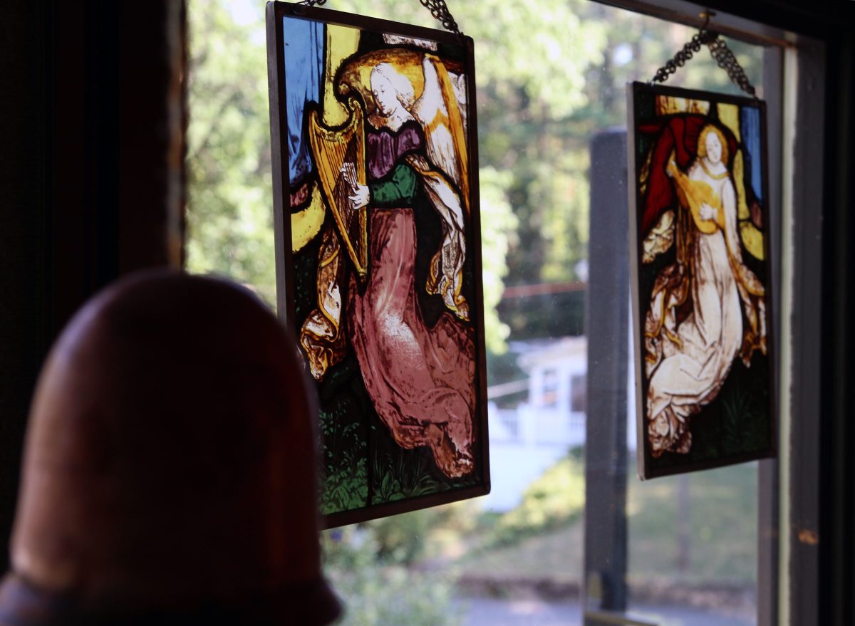 Framed stained glass paintings of angels suspended in front of one of the windows in Juliana Hall's house.