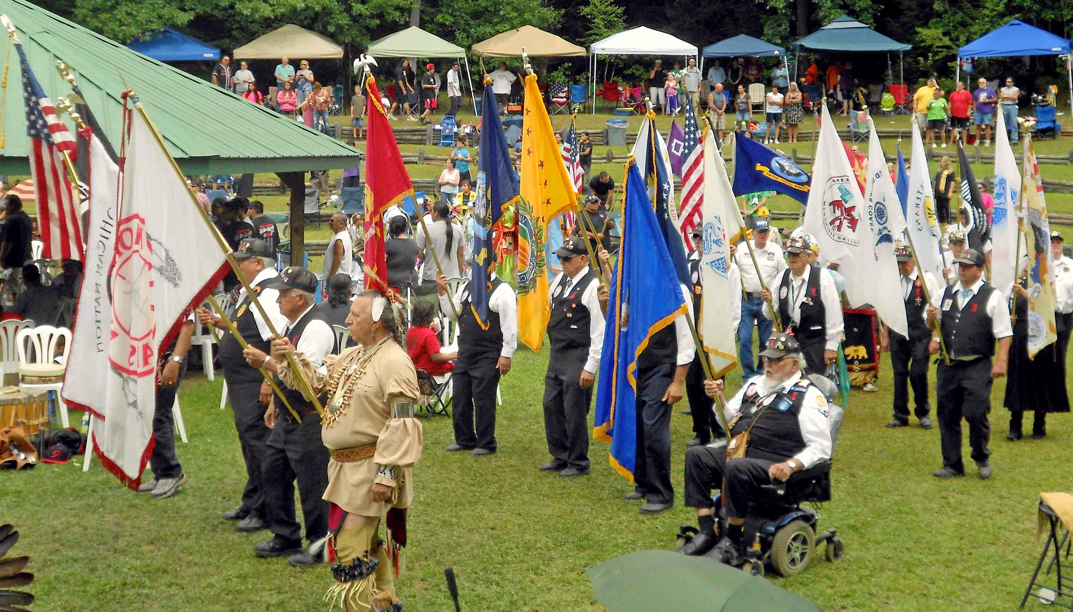 Mohican Nation elders outdoors marching with flags at a powwow.