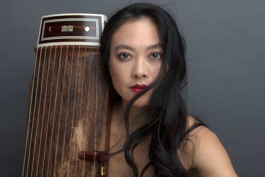 Jen Shyu with her hair in front of part of her face and a guzheng (classical Chinese zitrher) leaning against her right shoulder.